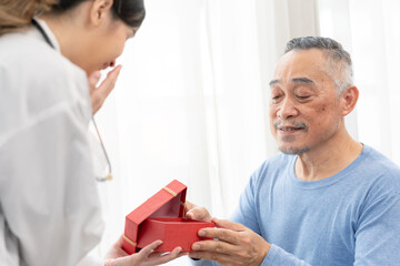 senior man receives a gift box from asian female doctor for happy birthday.