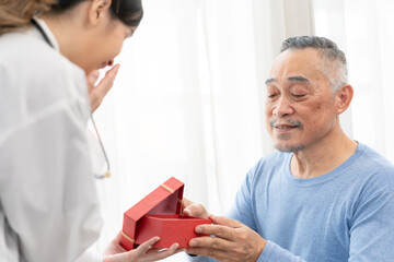 Obraz premium senior man receives a gift box from asian female doctor for happy birthday.