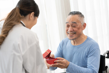 Obraz premium senior man receives a gift box from asian female doctor for happy birthday.