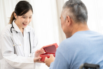 senior man receives a gift box from asian female doctor for happy birthday.