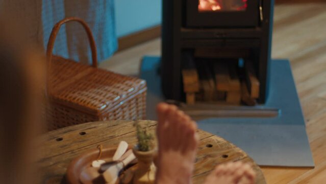 Woman relaxes in the house near the burning wooden stove and warms up her feet
