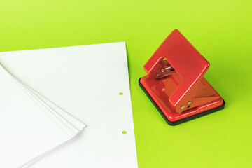 White writing paper and a red hole punch on a green background.