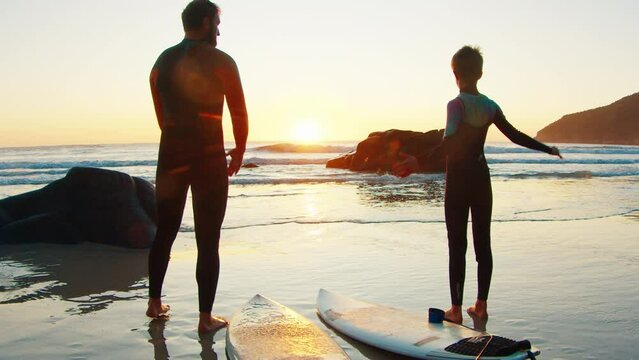 Family surf. Father and son go surfing at sunrise and do warm up exercises on the beach