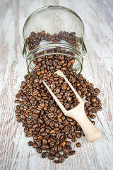 Top capture of coffee beans coming out of a glass jar and wooden shovel to catch them.