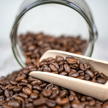 Macro photo of coffee beans on a wooden shovel and glass jar.