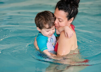 Little boy is getting used to the water in the pool being held by his mom