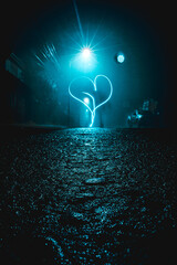 Corazón grande dibujado con luz en la noche sobre la calle de pavimento y piedras con luz azul del poste