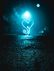 Corazón grande dibujado con luz en la noche sobre la calle de pavimento y piedras con luz azul del poste