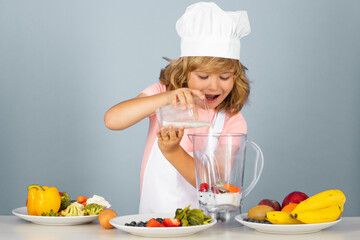 Kid boy in chef hat and apron cooking milk shake smoothie. Little cook with vegetables at kitchen. Natural kids food.