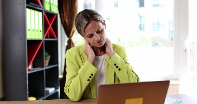 Woman at workplace with laptop takes break touches neck and suffers from pain caused bad posture