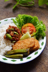 a plate of rice served with sambal and vegetables  