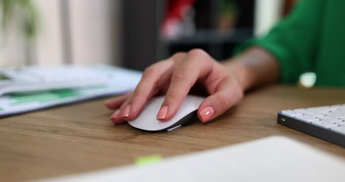 Closeup of woman hand holding a mouse and working with desktop computer sitting at office desk
