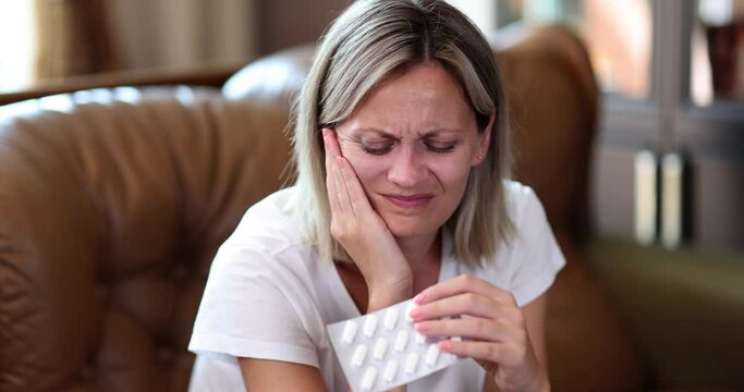 Woman touching face suffering from toothache and holding pill at home
