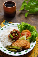 a plate of rice served with sambal and vegetables  