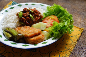 a plate of rice served with sambal and vegetables  