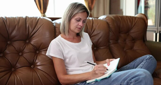 Pretty woman writes in notebook on sofa at home in living room