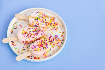 Bright and colorful flat lay of pink strawberry Popsicle ice cream with mint on blue background. Healthy summer food concept. Top view of popsicle with sprinkles, overhead