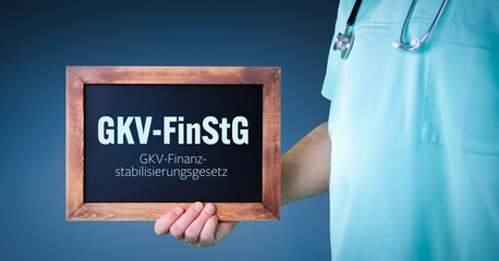 GKV-FinStG (GKV-Finanzstabilisierungsgesetz). Arzt zeigt Schild/Tafel mit Holz Rahmen. Hintergrund...
