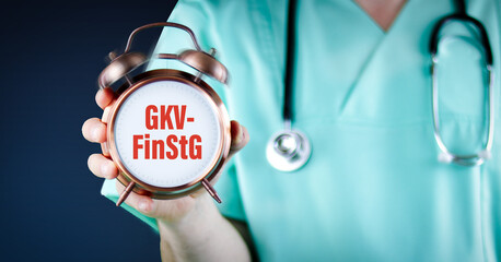 GKV-FinStG (GKV-Finanzstabilisierungsgesetz). Arzt zeigt Wecker/Uhr mit Text. Hintergrund blau.