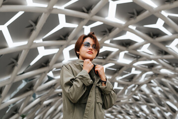 Stylish Asian model wearing eyeglasses and casual clothes posing against modern geometric design outdoors. Portrait of young woman with short haircut looking at camera