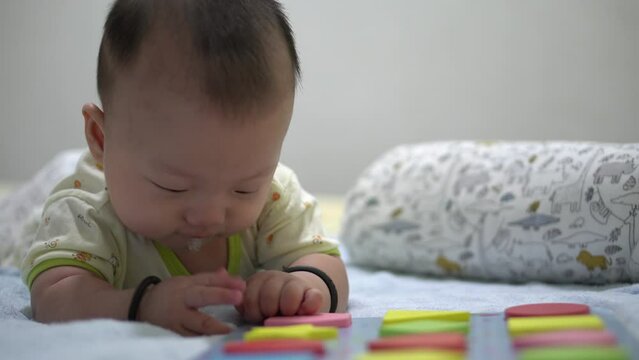 Asian baby lay down beside shape block sorting toy. Early preschool education concept
