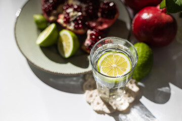 classic still life. ripe pomegranates and lime lie on a plate next to a vase with a red rose..