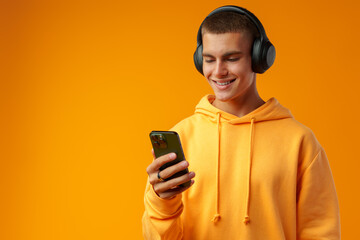 Young man listening music with headphones holding mobile phone against yellow background