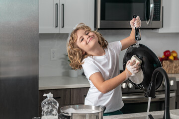 Funny child help in washing dishes at kitchen. Dishwashing liquid bottle on kitchen sink and clean plates.