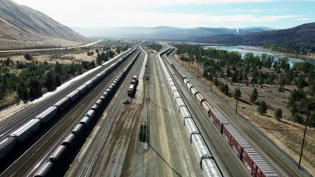 forward flight dolly drone shot flying over a railroad station in a desert environment on a sunny day next to a highway and a river and mountains in the background and powerines in the picture