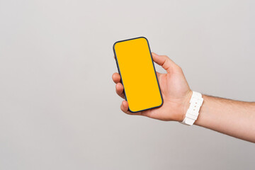 Close up photo of male hand holding smartphone with blank screen for copyspace over grey background.