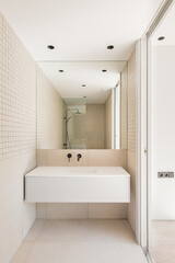 Modern bathroom with beige tiles. shower zone with glass partition reflected in the mirror