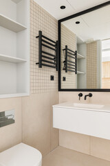 Naklejka na ściany i meble Interior of modern bathroom with beige tiles. Black framed mirror, radiator, toilet and white sink