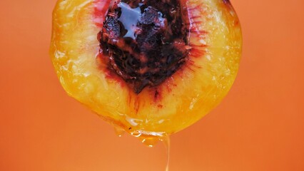 cut peach with juice dripping on an orange background - obrazy, fototapety, plakaty