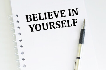 BELIEVE IN YOURSELF text on notepad on a white table next to it lies a pen, a business concept