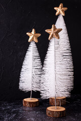 Christmas postcard. Decorative white holiday trees with golden stars  on  black textured background. Scandinavian minimalistic style. Still life. Place for text.
