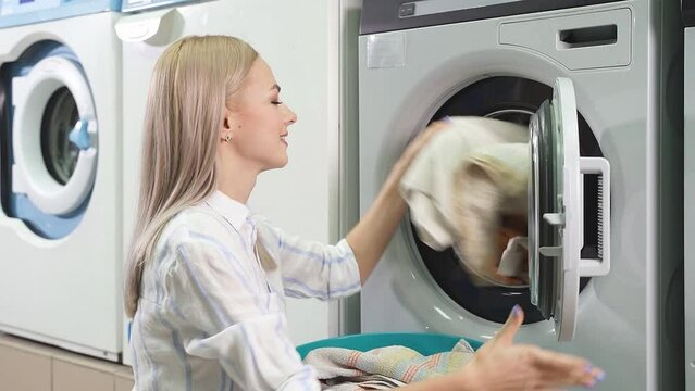 An attractive blonde takes clean laundry out of a washing machine in a public laundry room