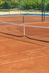 Baseline and net of an empty clay tennis court on a sunny day