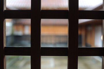 Wooden bars or grilling in a window of a traditional japanese building with view on a courtyard and tile roof