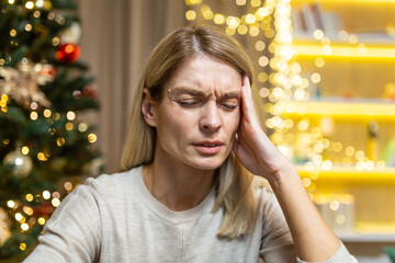 Close-up photo portrait of mature woman lonely and depressed on Christmas, thinking wife sitting on sofa near Christmas tree in living room, on New Year holidays alone.