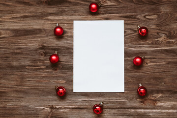 Naklejka na ściany i meble A blank sheet of paper and and red Christmas balls on a wooden background. Top view, flat lay