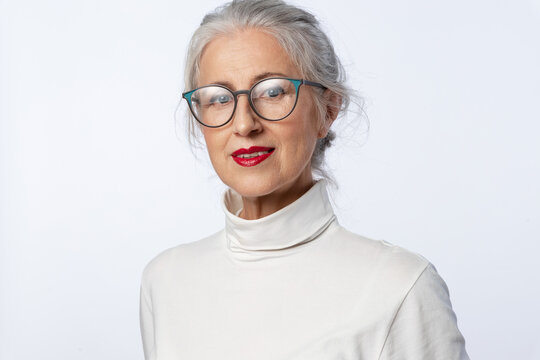 Lovely elderly woman with slight smile on her brightly painted red lips and clean, well-groomed skin, wearing glasses, looks at the frame on white background