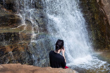 Obraz premium a tourist girl sits on a rock or admires Gadelsha, the largest waterfall in the Southern Urals, on a spring sunny day on the Irendyk ridge.