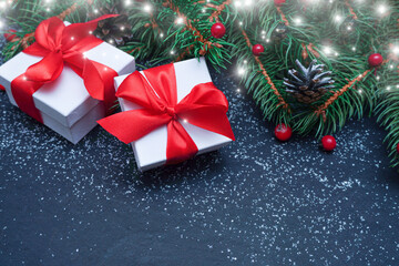    Spruce, fir branches, red berries, gift box on black stone background. Frame border. Christmas New Year composition background. Christmas lights. Space for text