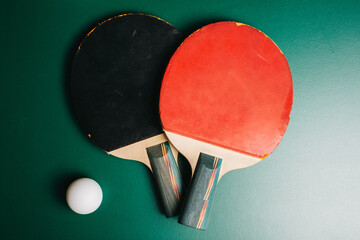 Two ping pong rackets and a ball are on the green game table