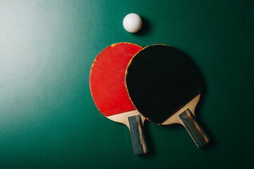 Two ping pong rackets and a ball are on the green game table