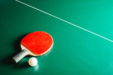 Ping pong racket and a ball are lying on a green game table