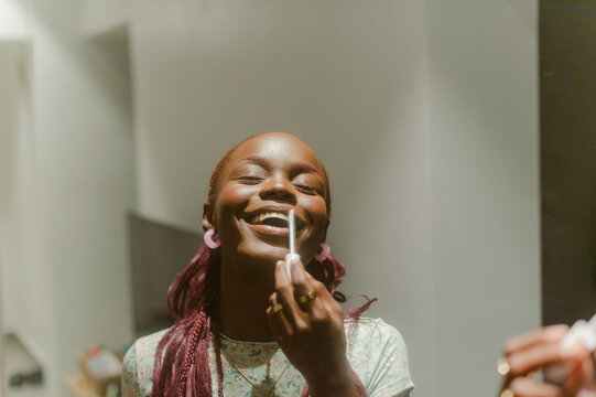 A black woman smiling and applying make-up