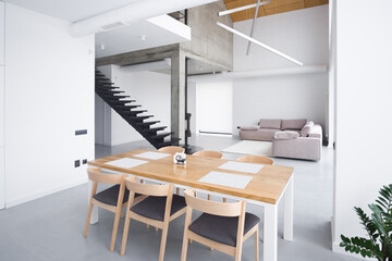 Fototapeta na wymiar Elegant white kitchen interior with a large spacious sofa against the backdrop of a staircase without people. Stylish wooden table in the kitchen. front view of kitchen table, minimalism. Kitchen