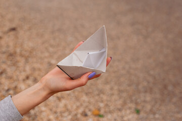 hand with Small paper boat from paper on sand near sea waves. Concept paper boat on a sandy beach...