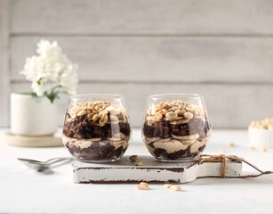 Dessert in glasses, chocolate biscuit with peanut cream, banana and nuts on the white table 